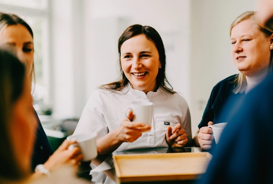 Zahnärztin Dr. Simona Braun tauscht sich be einem Kaffee mit ihren Mitarbeiterinnen aus.