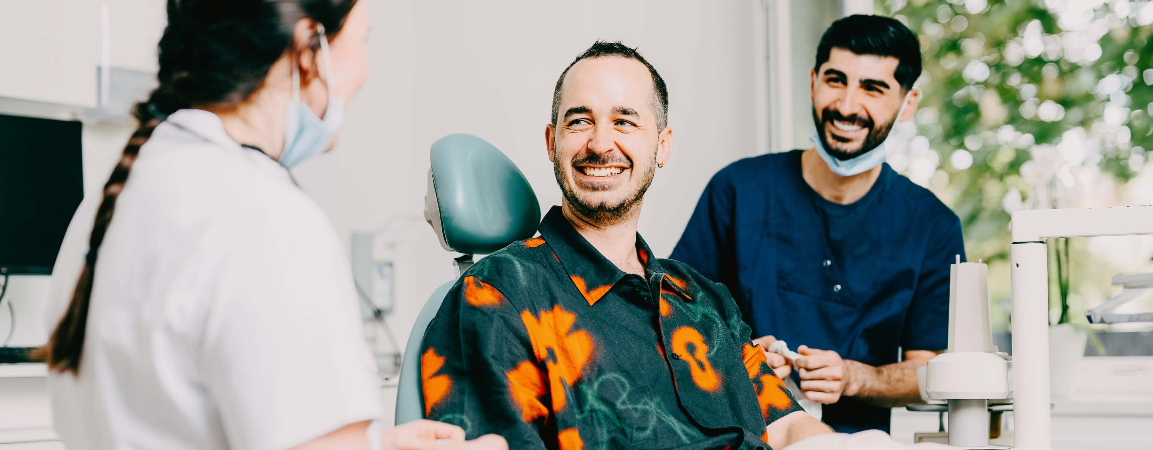 Zahnärztin Dr. Simona Huber und Auszubildender Ramadhan im Gespräch mit einem Patienten